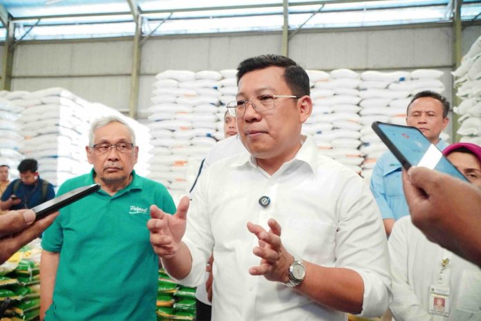 Arief Prasetyo Adi, Kepala Badan Pangan Nasional, memberikan keterangan kepada media di gudang beras, dengan latar belakang tumpukan karung beras.