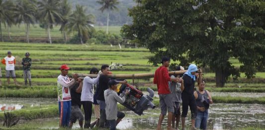 petani menggotong mesin pompa air